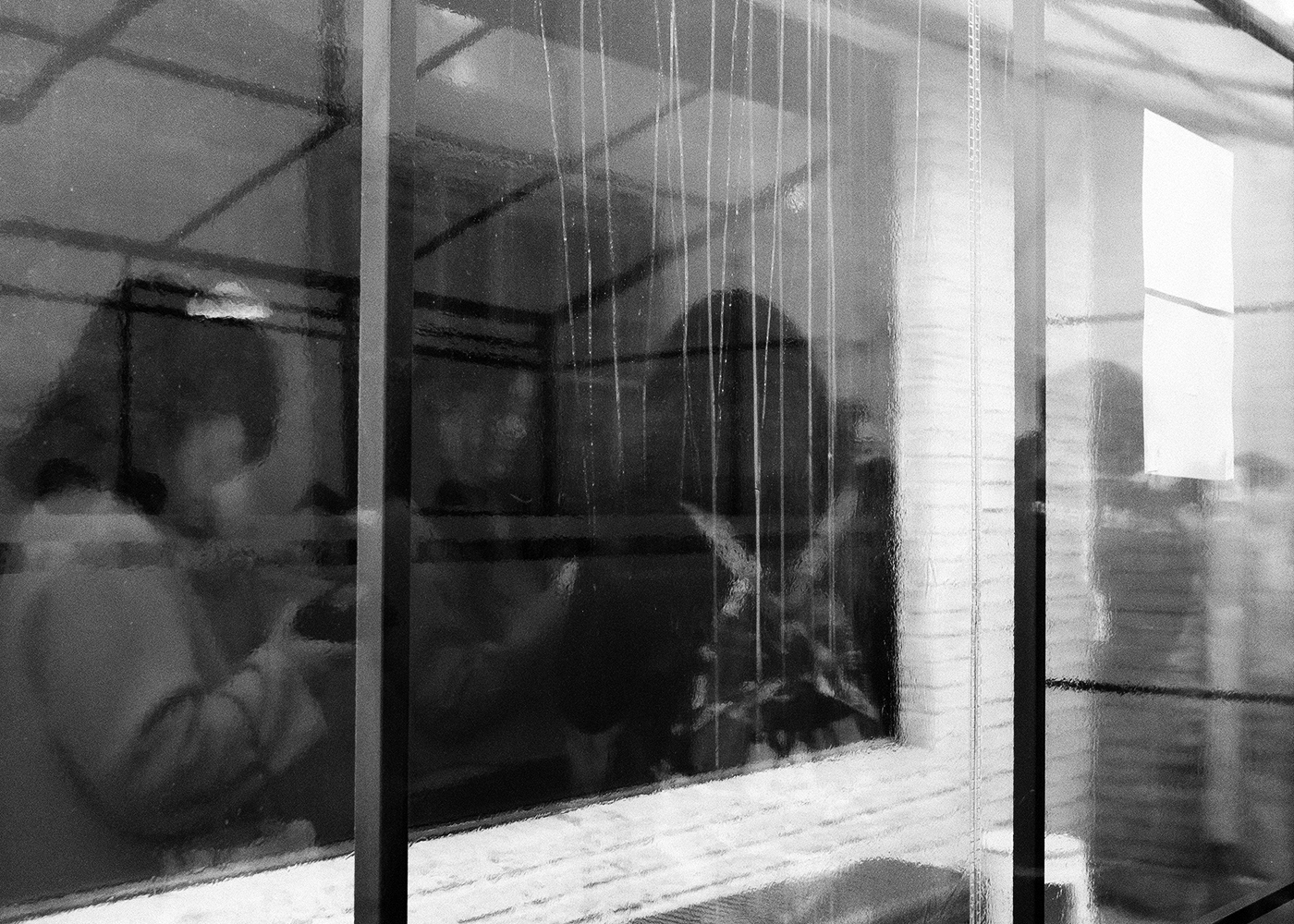 Blurred figures in a café seen through rain-streaked textured glass